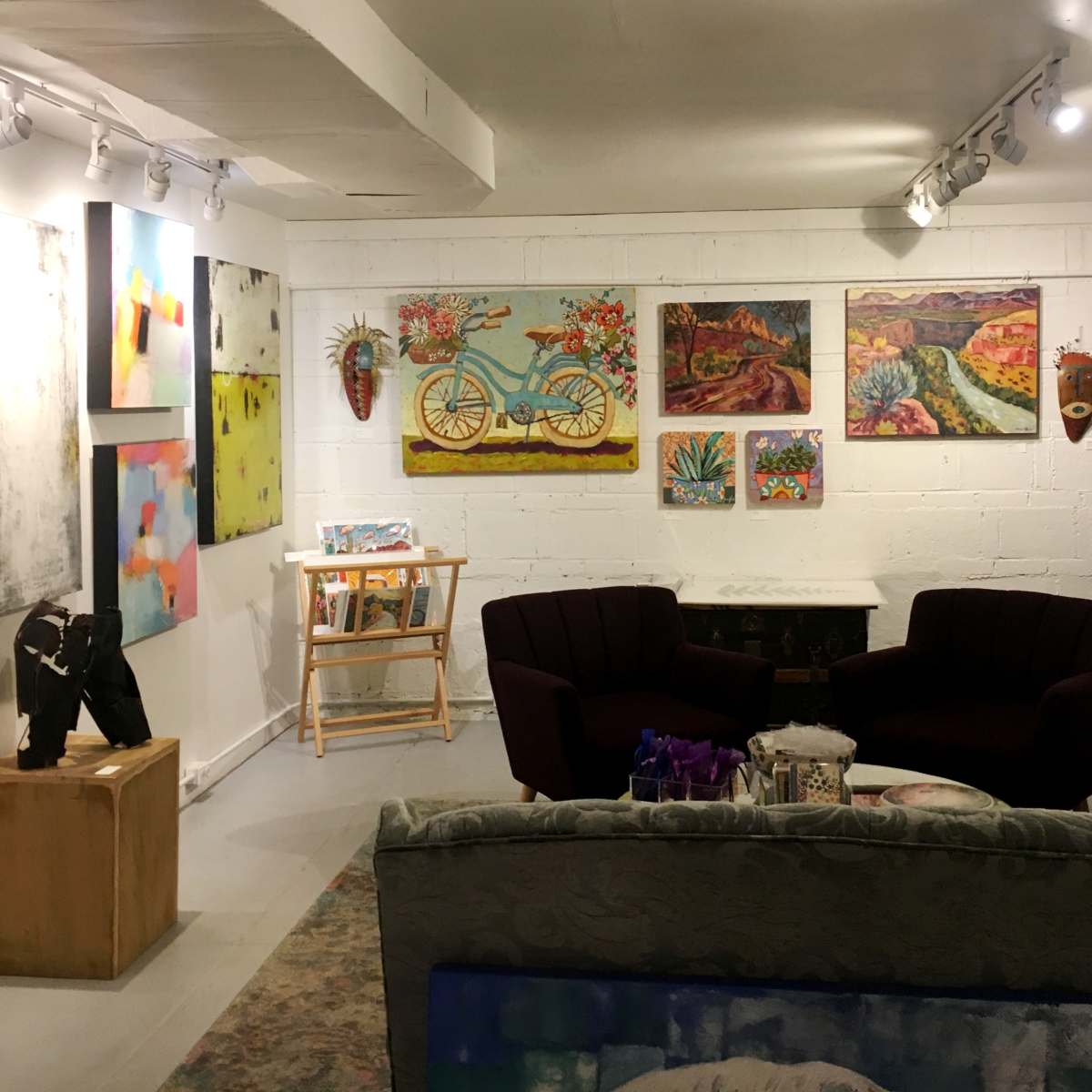 An art gallery featuring colorful paintings and sculptures displayed on the white walls and furniture of a well-lit room.
