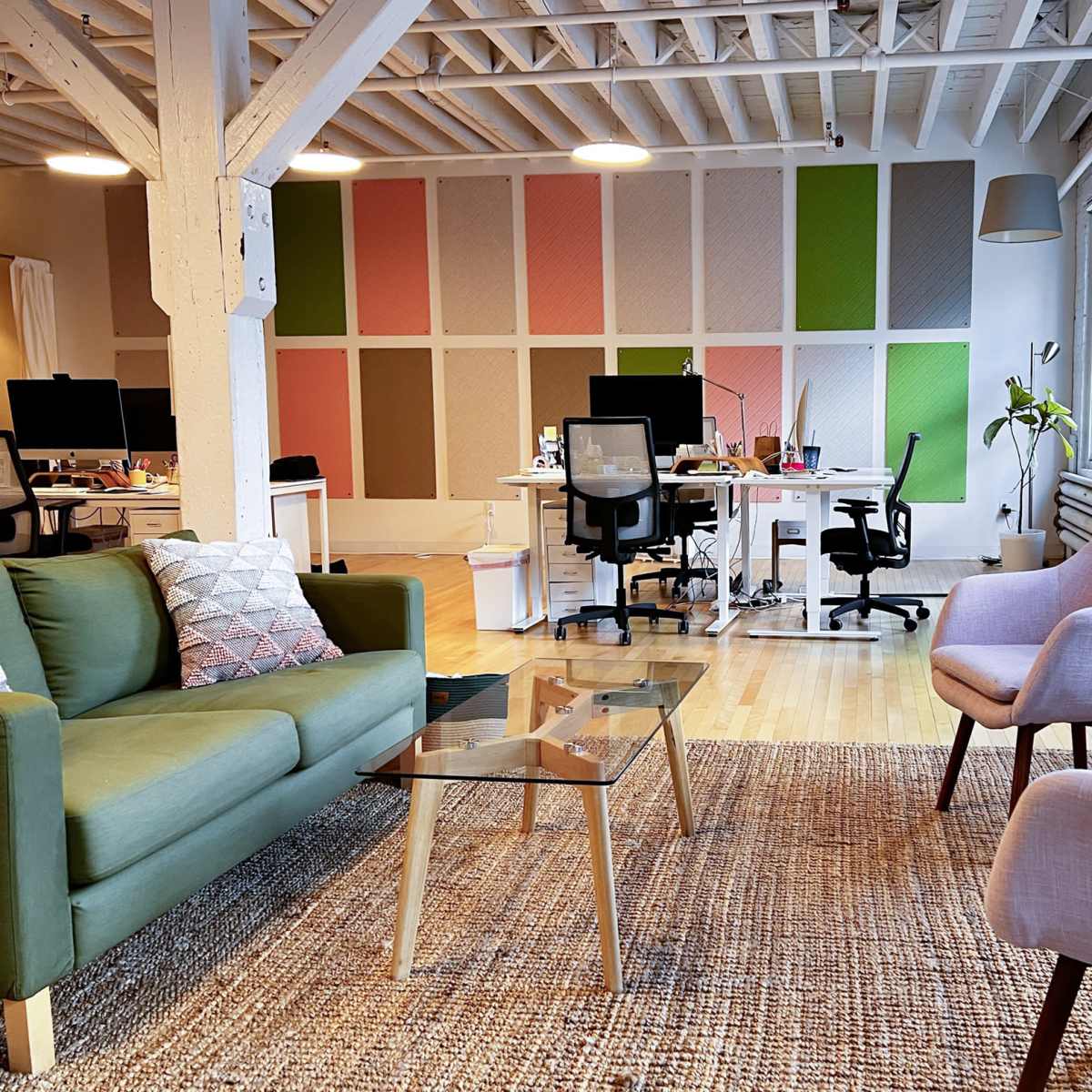 A bright office space featuring a green sofa and two light-colored chairs in front of workstations with computers and colorful wall decor.