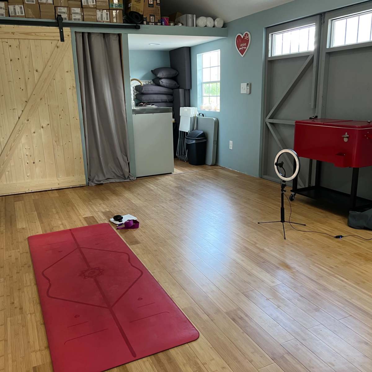 The room features a yoga mat on the wooden floor, surrounded by battery-operated candles, with storage boxes stacked in the corner and a small mirror setup for viewing.