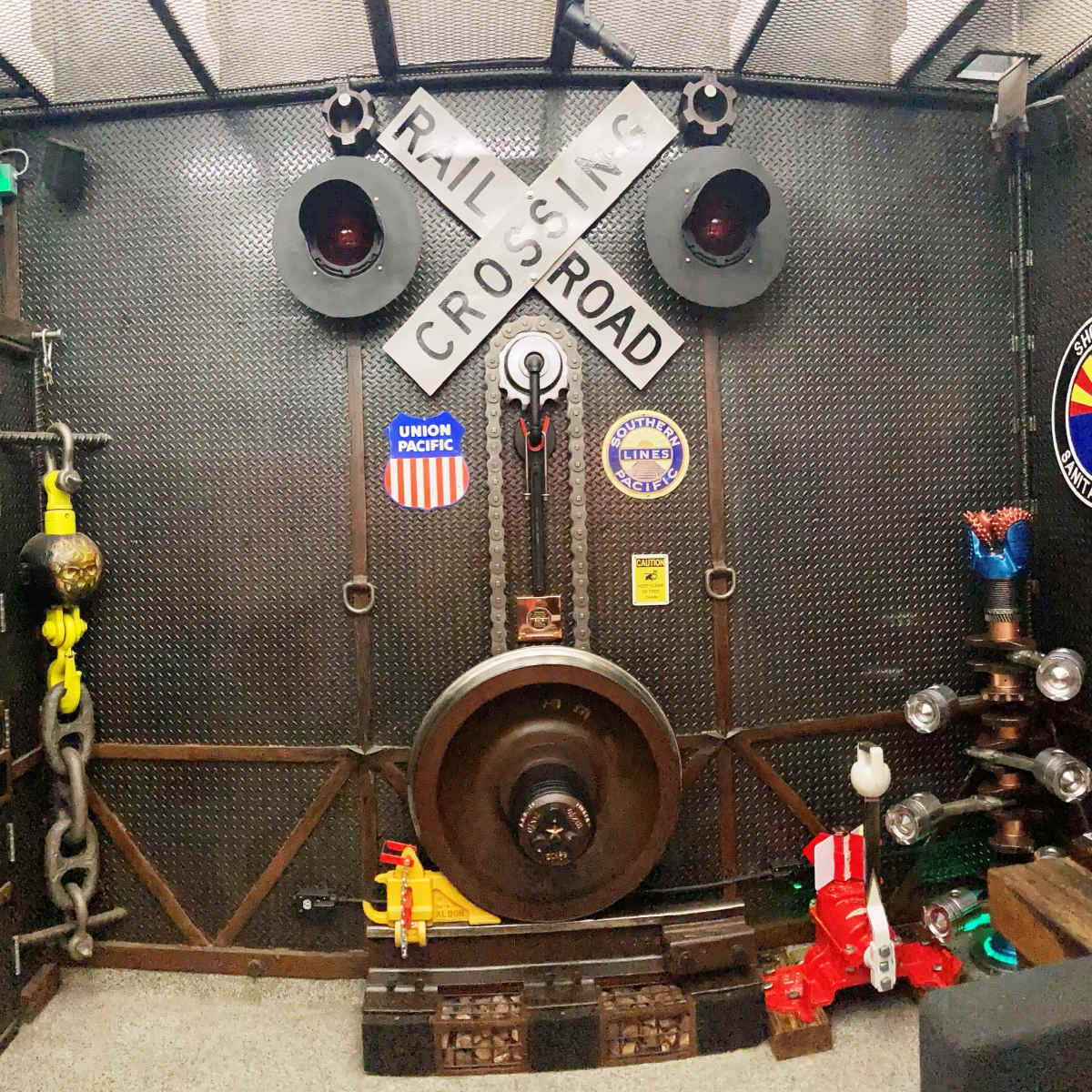 A wall featuring a railroad crossing sign, traffic lights, and various railroad-themed decorations, including chains and a large wheel.