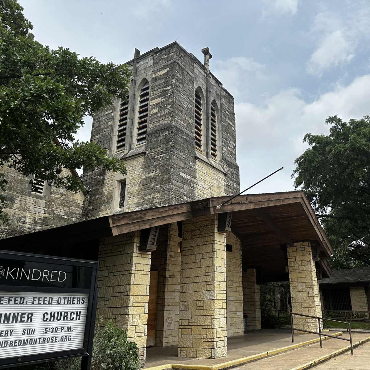 A stone church building with a tall bell tower and large trees surrounding it.