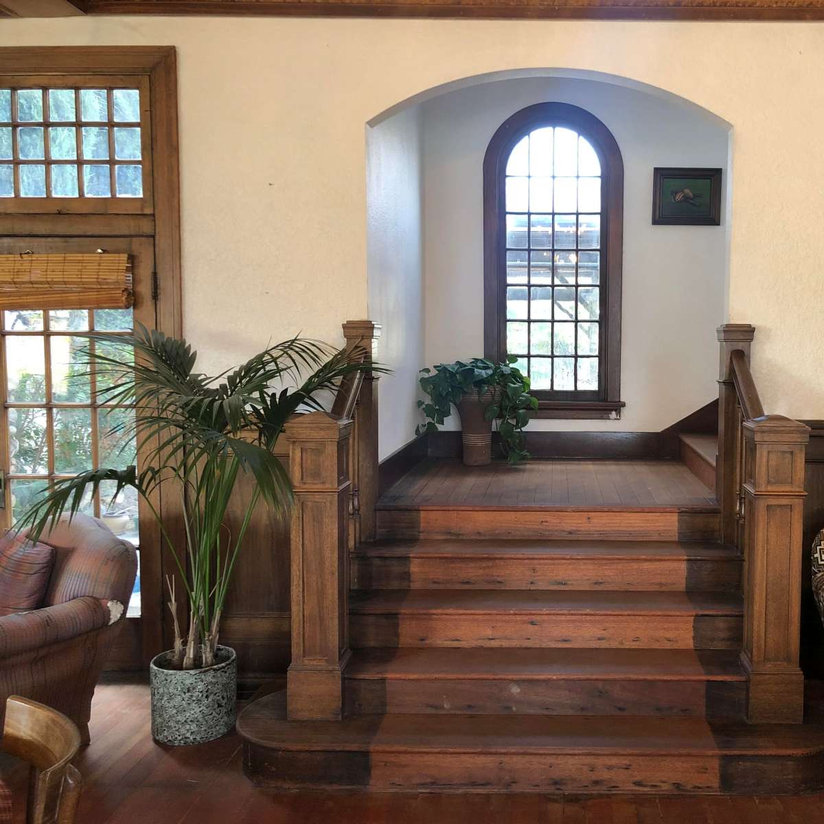 A staircase leading up to a landing with a large arched window and a potted plant on a ledge.