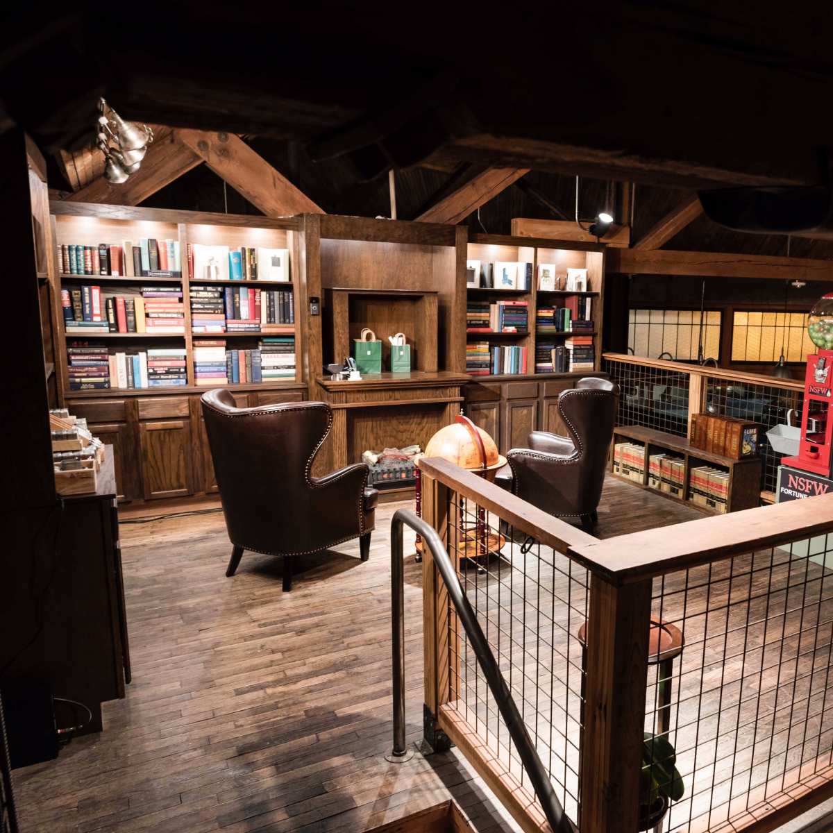 A cozy, wooden loft space with bookshelves, two armchairs, and a gumball machine.