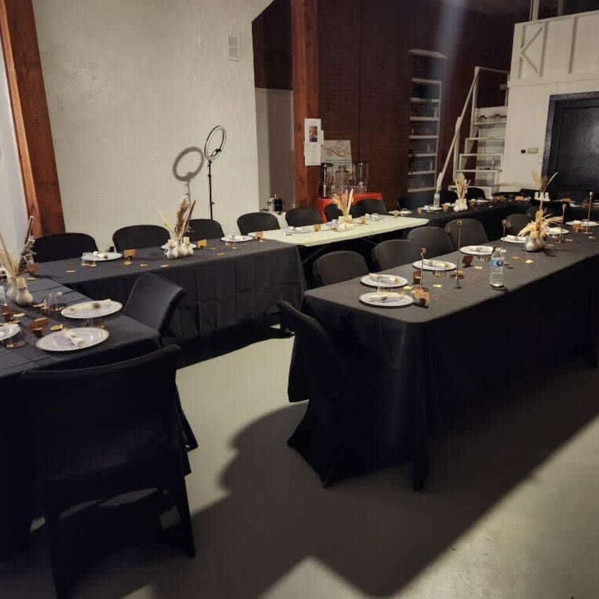 A spacious dining area set with black tables adorned with plates and decorative centerpieces.