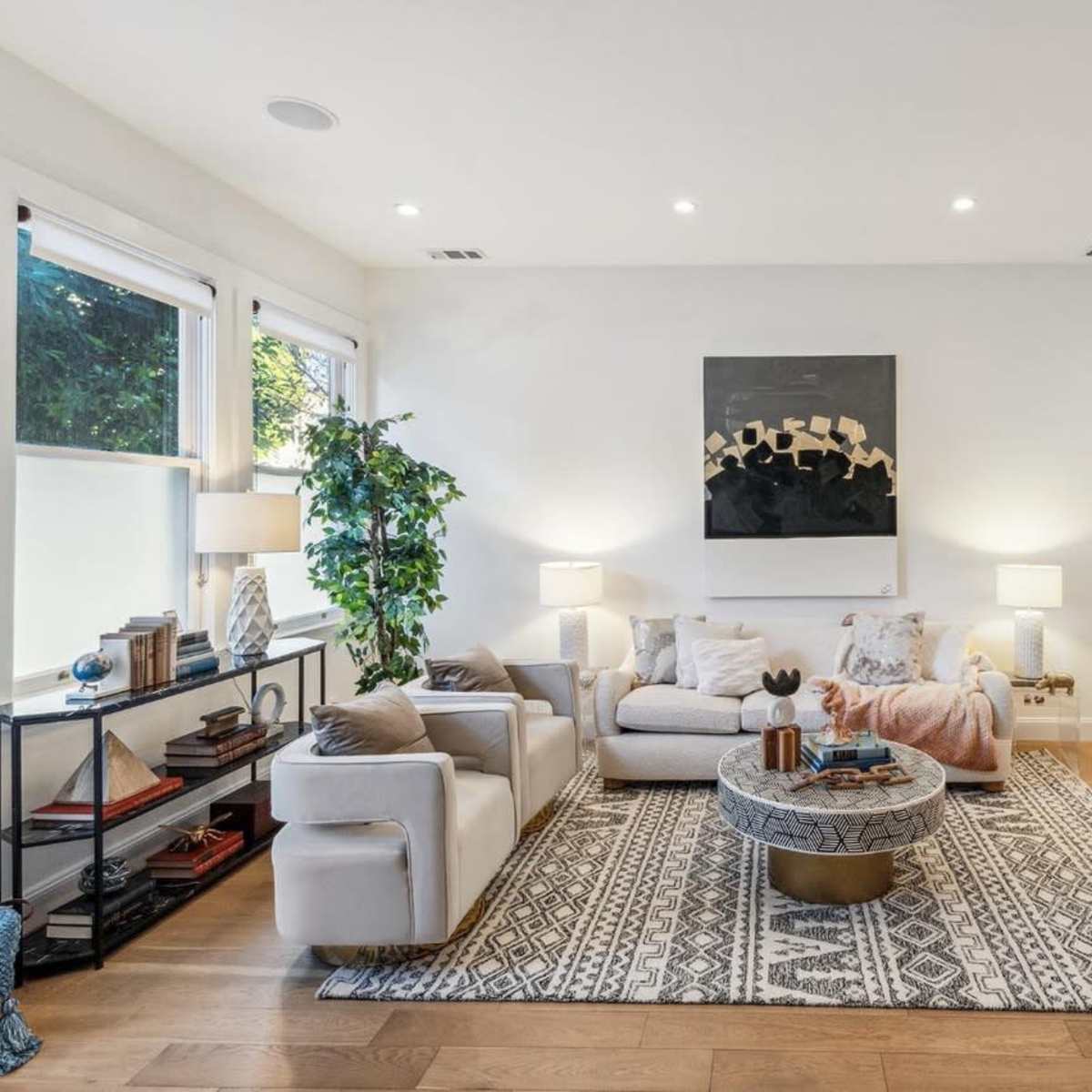 A modern living room with a neutral color palette, a large area rug, a round coffee table, and a dining area in the background.