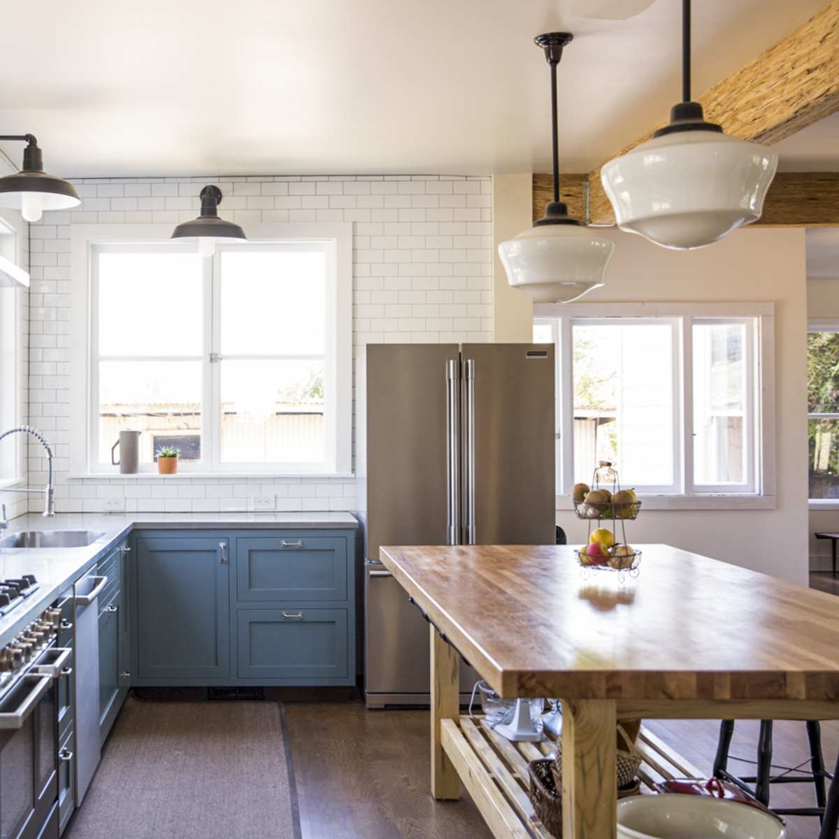 The kitchen features blue cabinets, stainless steel appliances, a wooden island, and large windows that provide natural light.