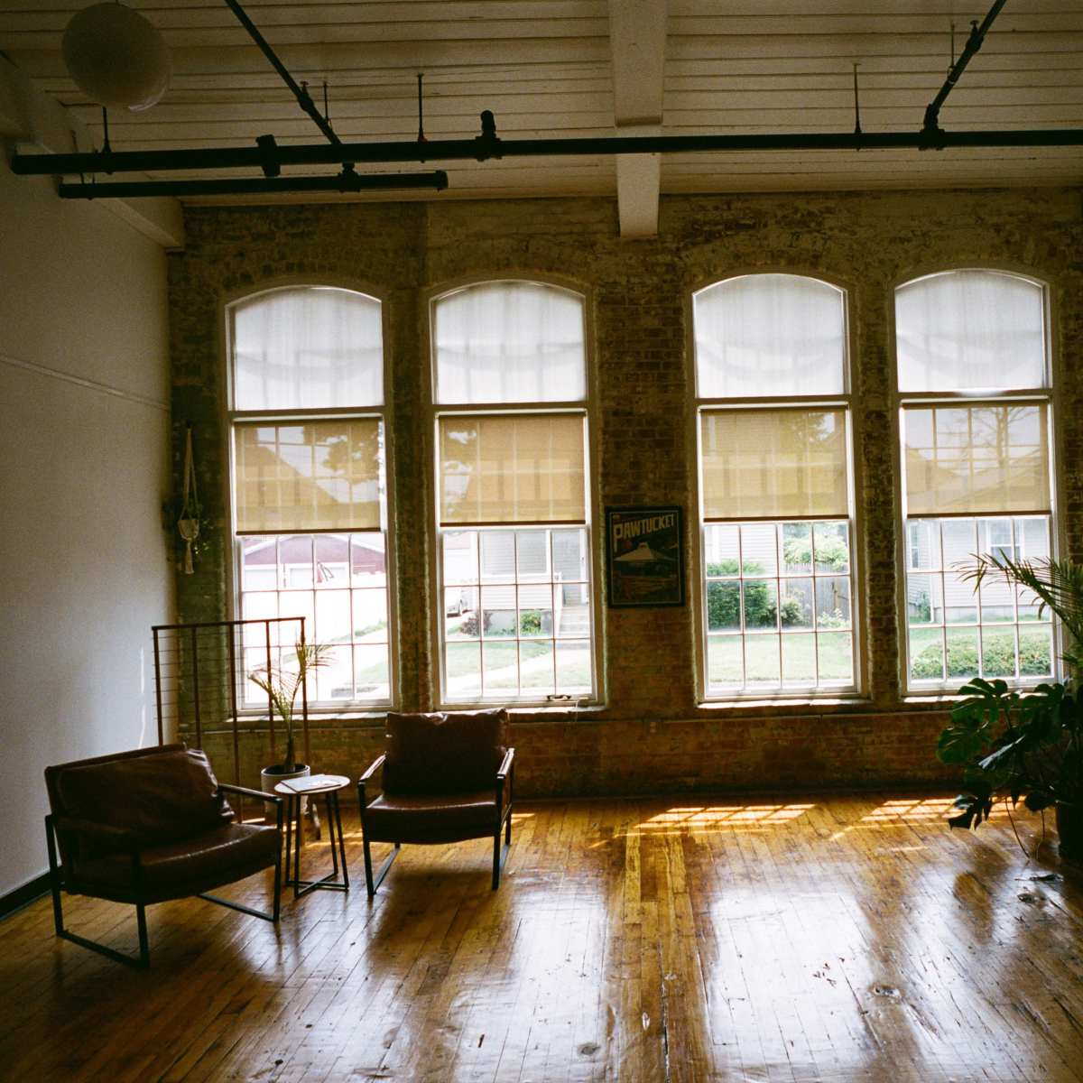 A minimalistic interior with two chairs, a small table, and large windows allowing natural light to illuminate the wooden floor.