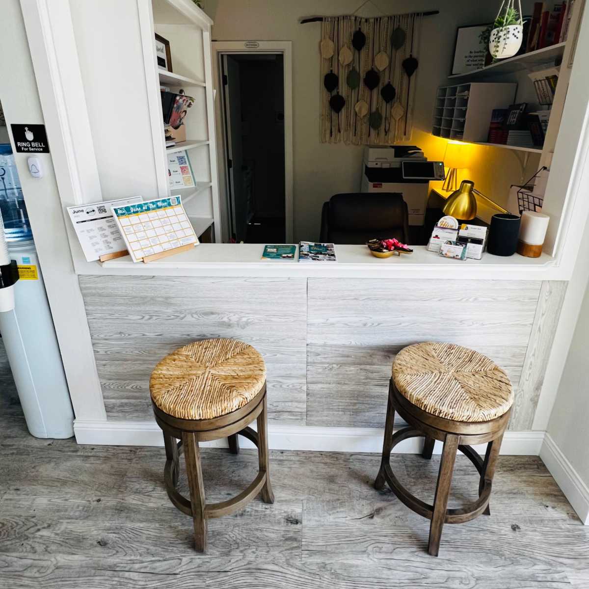 A small reception area featuring two woven stools and a counter with a calendar and paperwork on it.