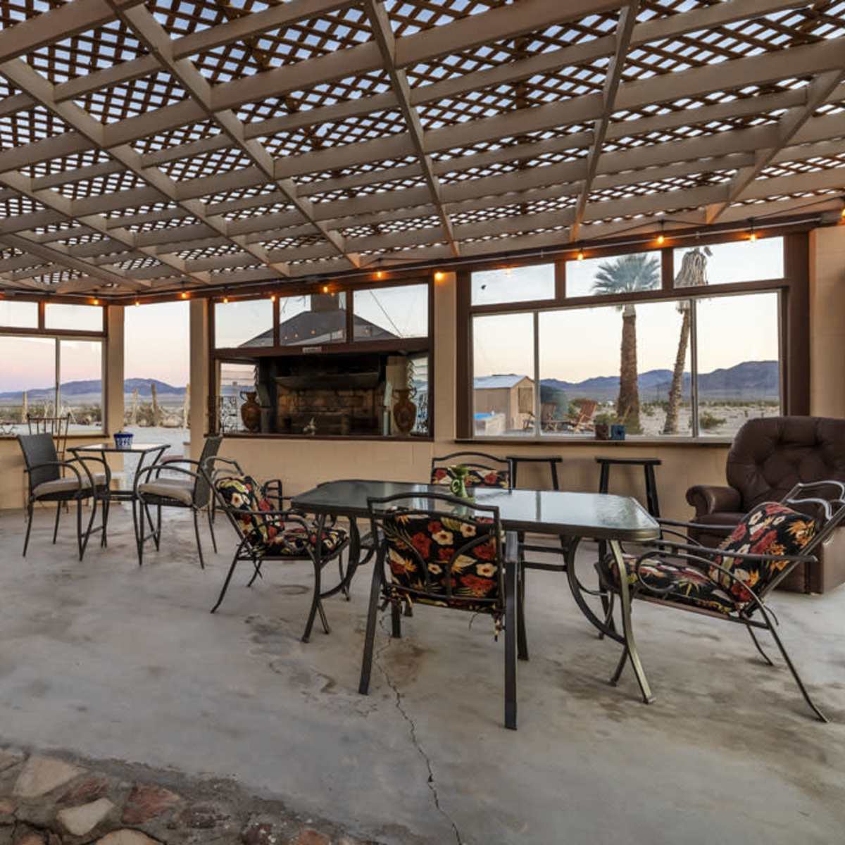 A spacious patio with metal furniture, a stone floor, and large windows overlooking a mountainous landscape.