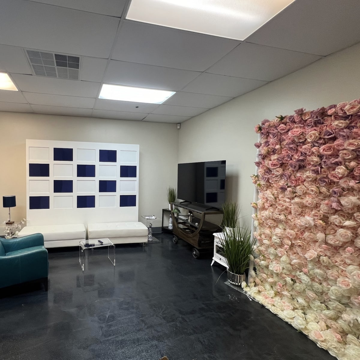 A modern room featuring a white sofa, a teal armchair, a large television, and a floral wall decoration made of roses.