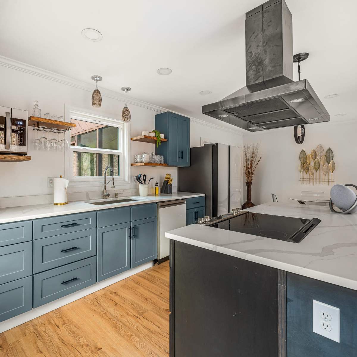 A modern kitchen with blue cabinets, a large island with a stovetop, a microwave above the counter, and a variety of appliances.
