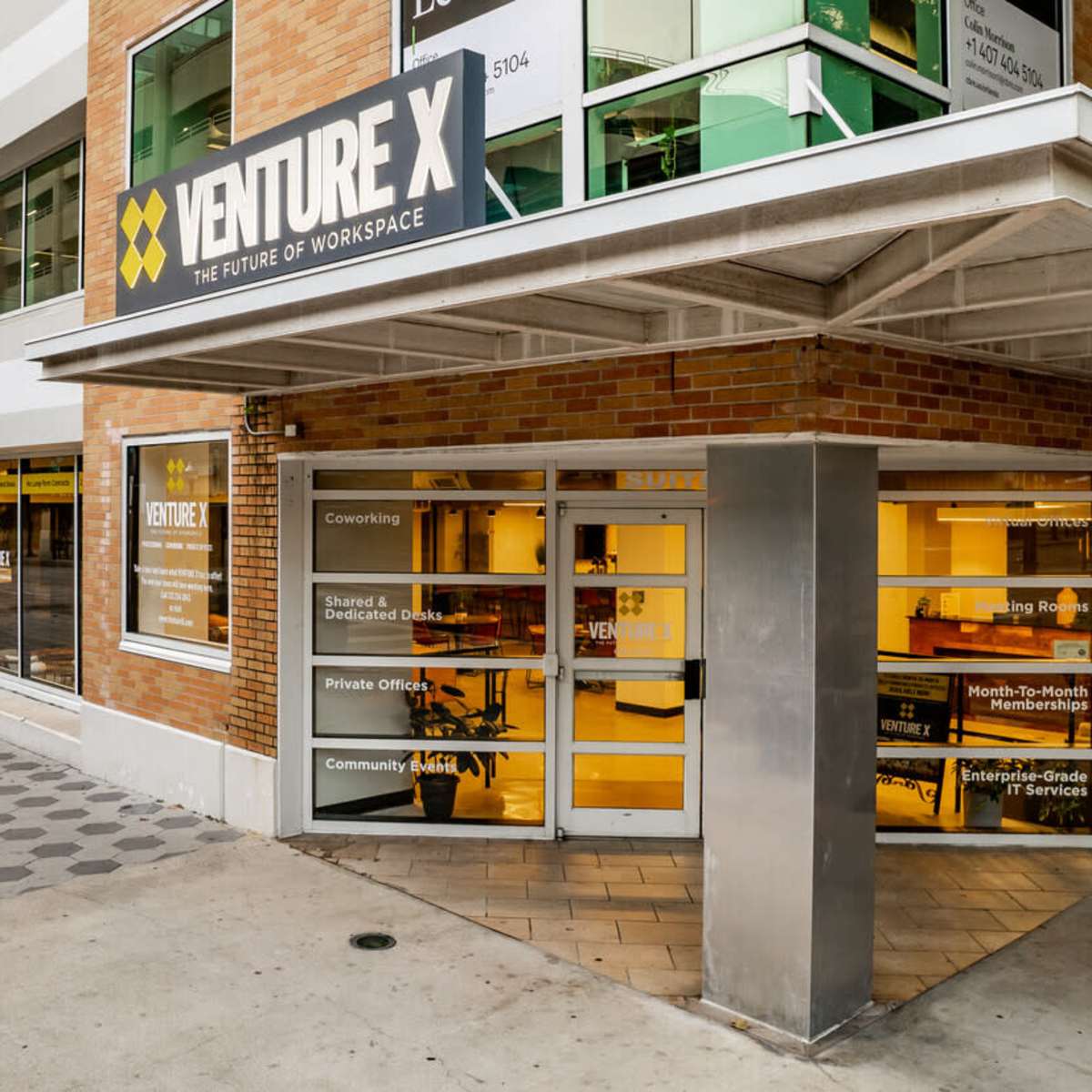The entrance of a modern coworking space called Venture X, featuring large windows and a sign overhead.