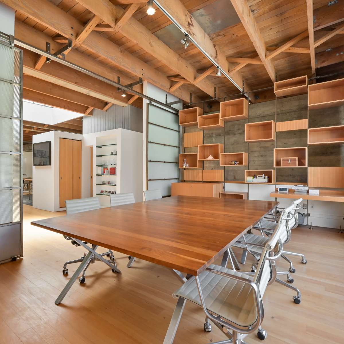 A modern office space with a large wooden table and sleek chairs, surrounded by wooden beams and shelving.