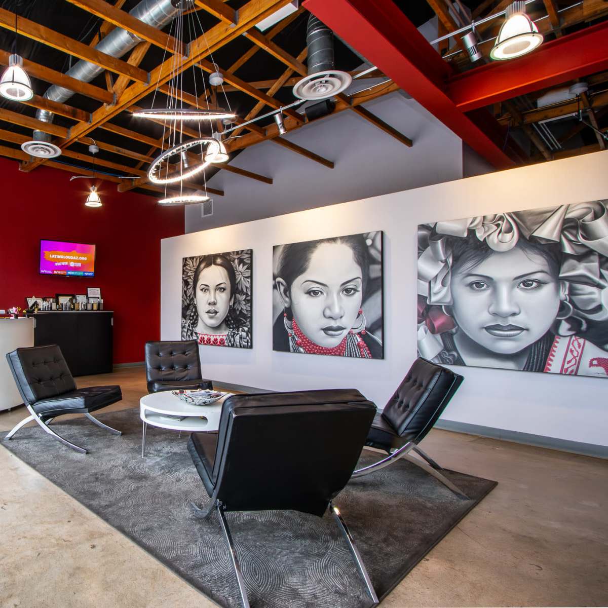 A modern reception area with a curved front desk, three large portraits on the wall, and black leather chairs arranged around a low table on a carpet.