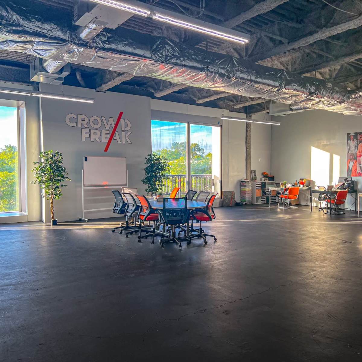 A spacious office interior with modern furniture, large windows, and a branded wall featuring multiple images.