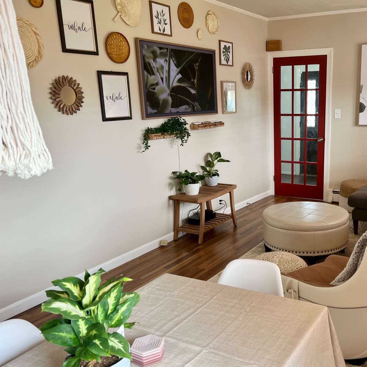A cozy living room features a mix of wall art, plants, a chaise lounge, and a red door leading to another space.