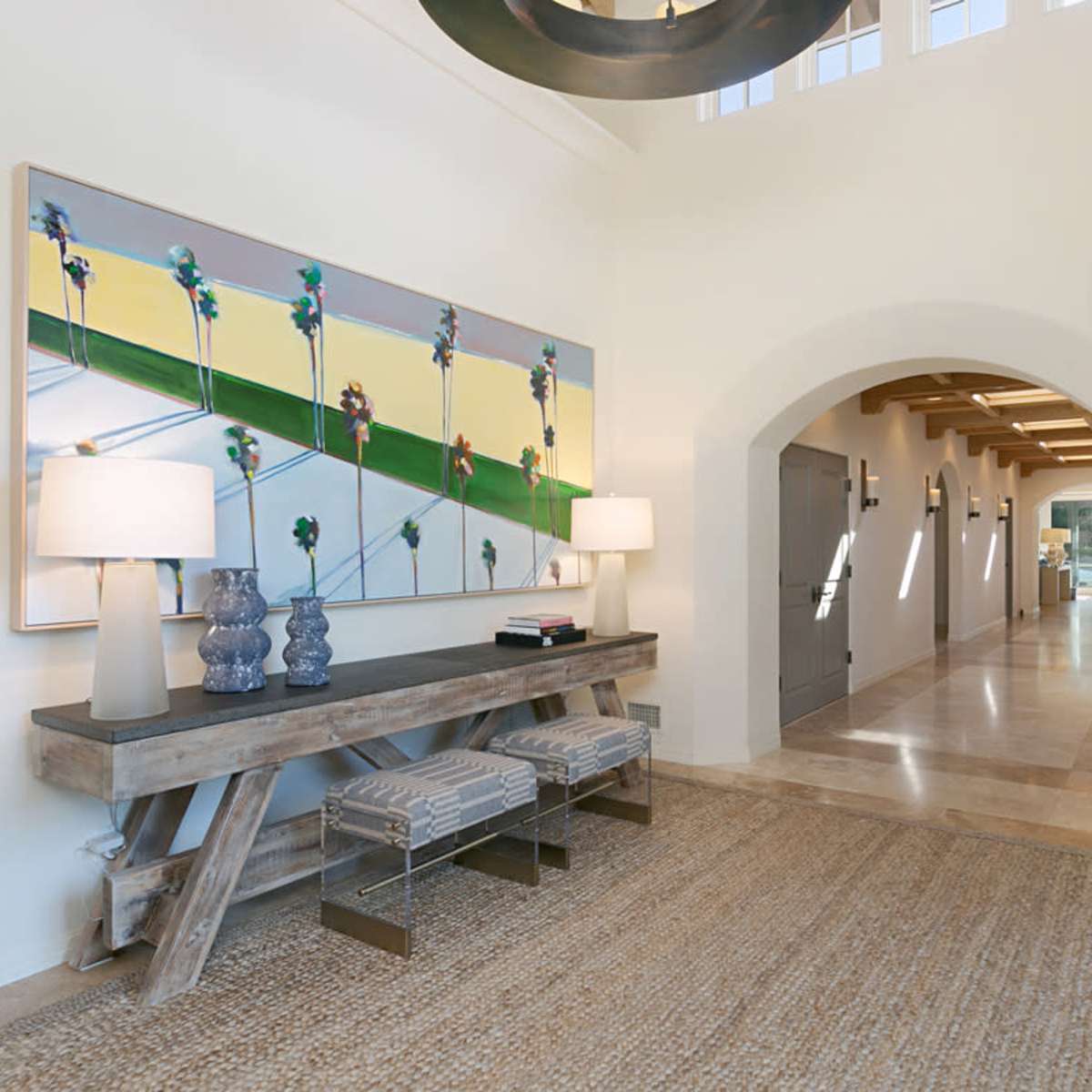 A well-lit hallway with a modern console table, two lamps, and a large artwork on the wall.