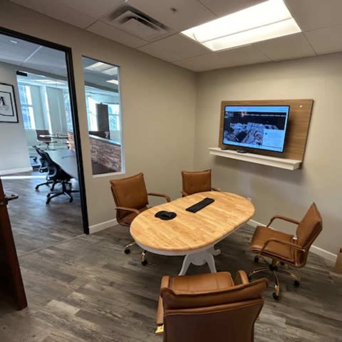 A small conference room features a circular wooden table surrounded by four chairs and a mounted television on the wall.
