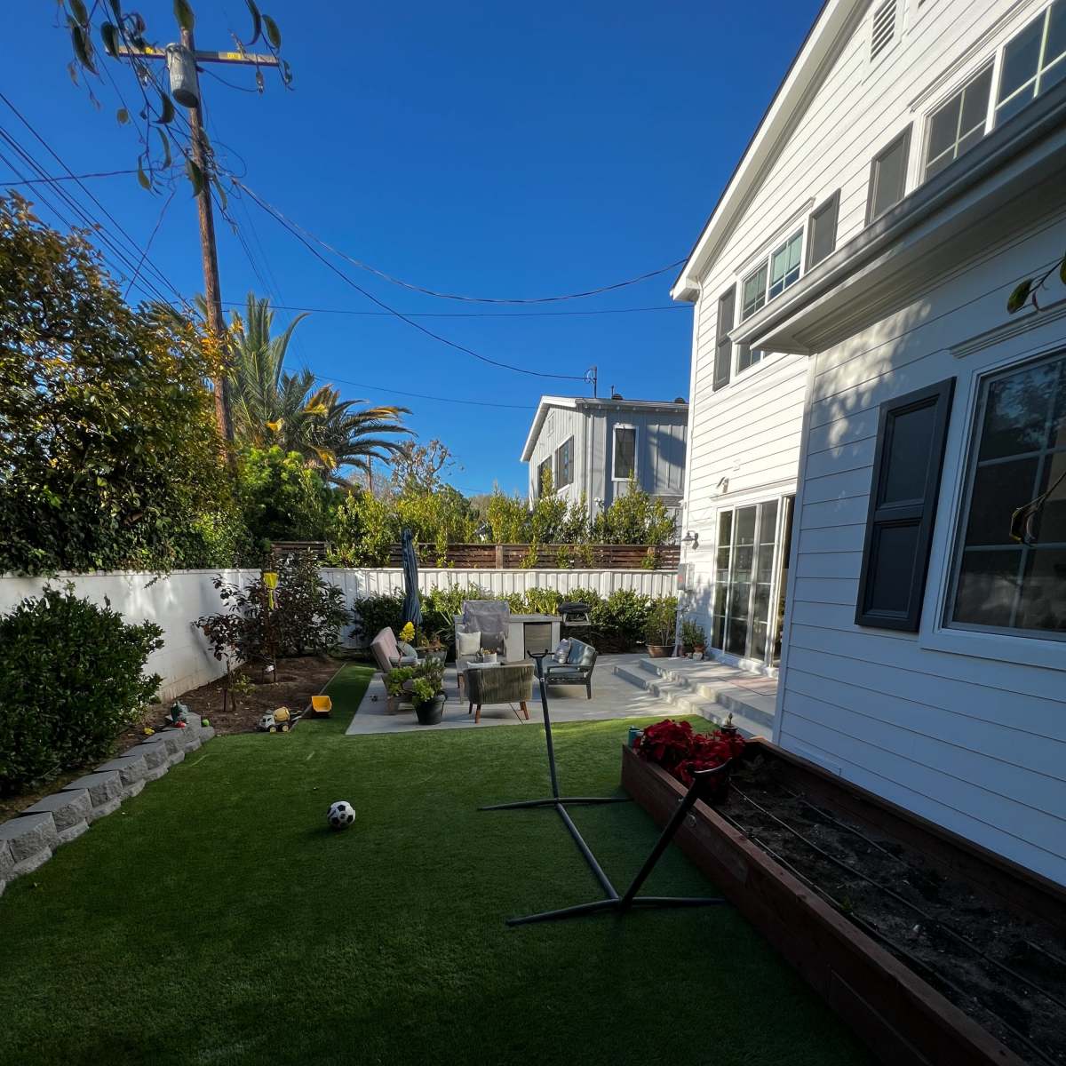 A backyard with artificial grass, a patio area with chairs and a table, and a small soccer ball on the ground.