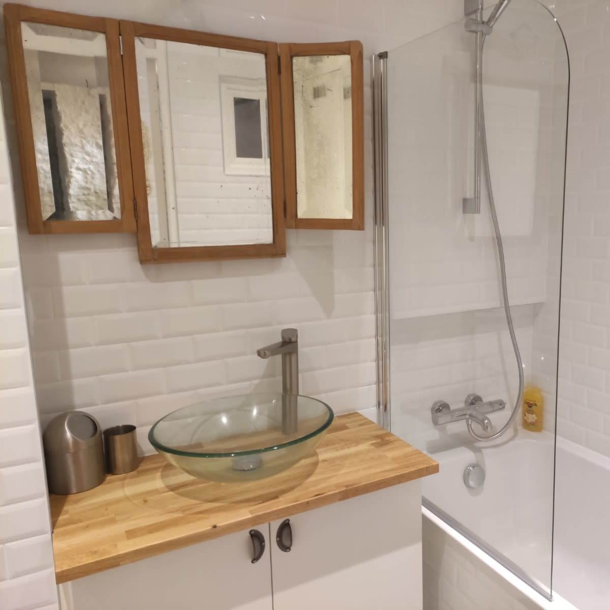 A modern bathroom with a glass shower enclosure, a wooden countertop, a vessel sink, and a mirror above the sink.