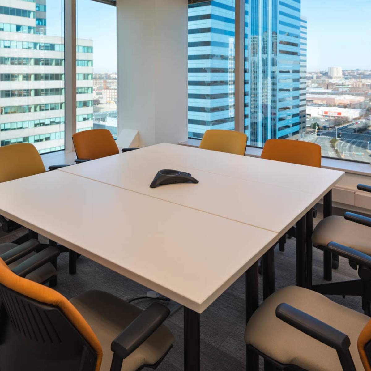 A conference room with a square table and eight chairs overlooks a cityscape through large windows.