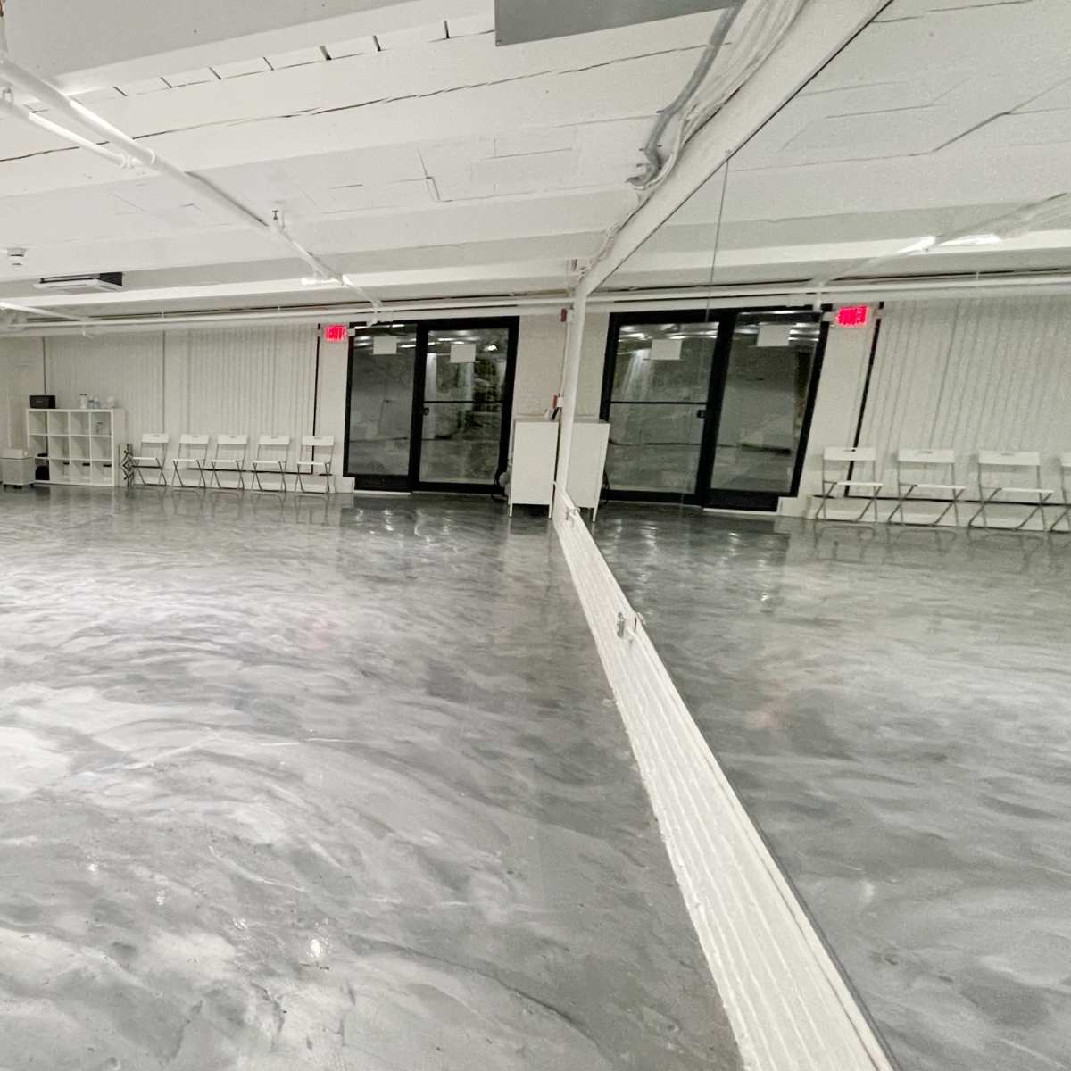 A spacious, empty studio with a polished gray concrete floor and large windows allowing natural light.