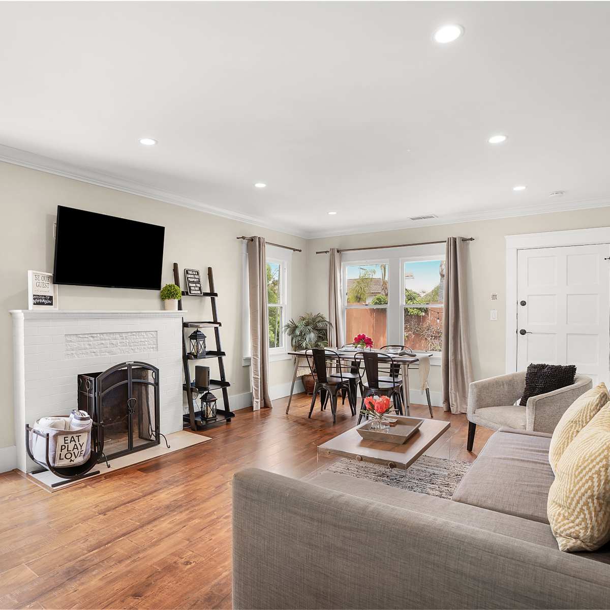 A living room with a gray sofa, a fireplace, a mounted television, and a dining table near a doorway leading outside.