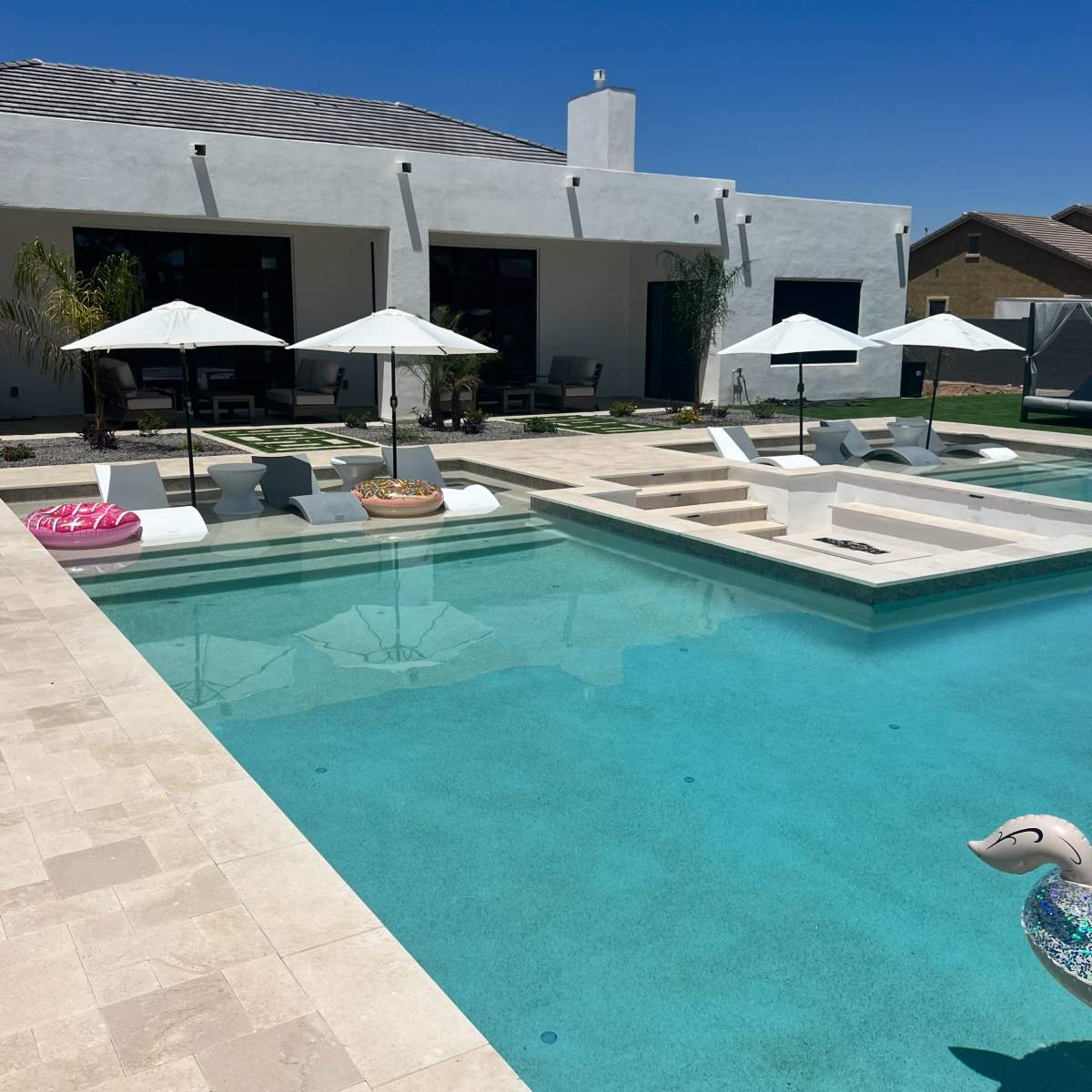 A swimming pool surrounded by lounge chairs and umbrellas, with a modern house in the background.