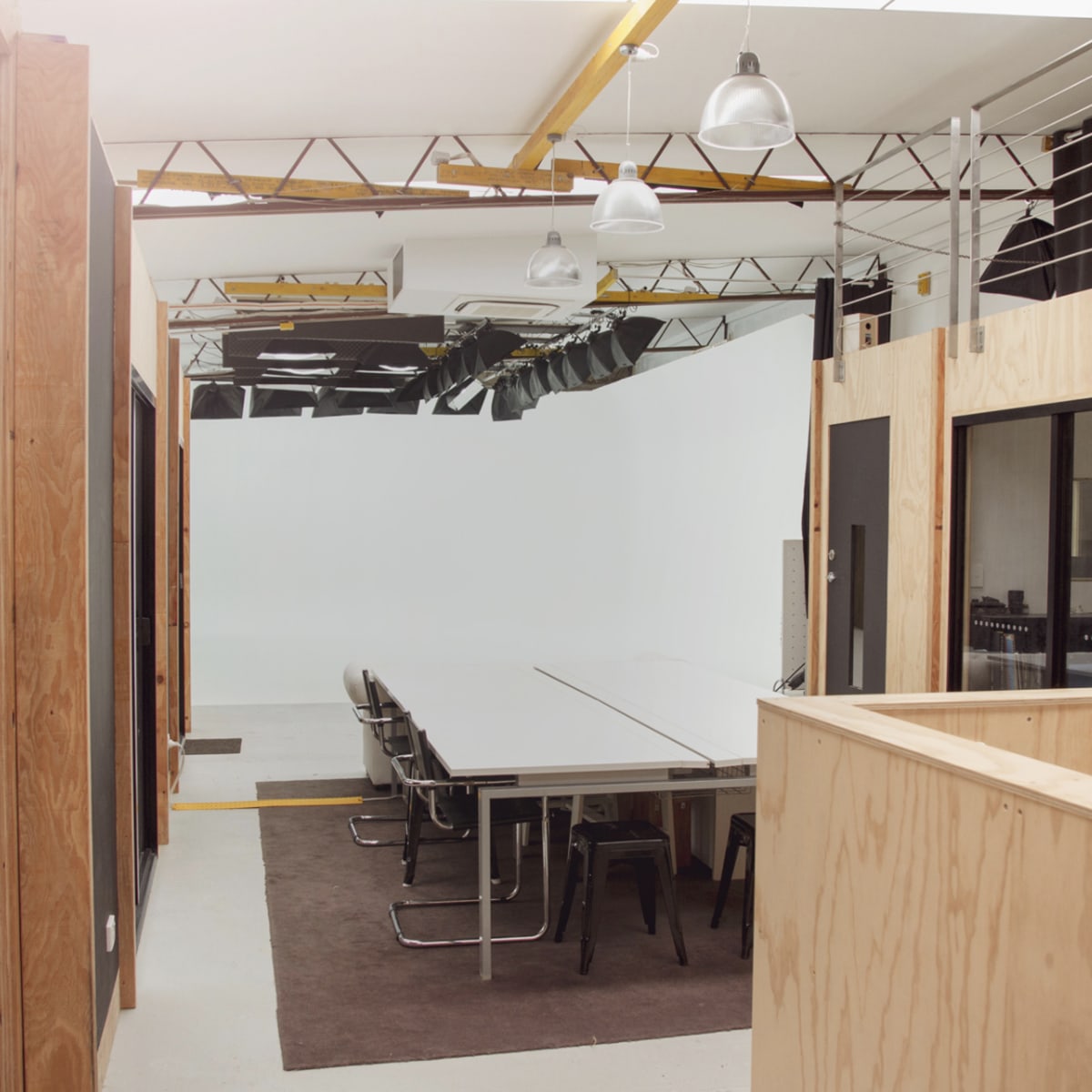 A modern office space featuring a long conference table surrounded by chairs, with wooden walls and a bright, open area.