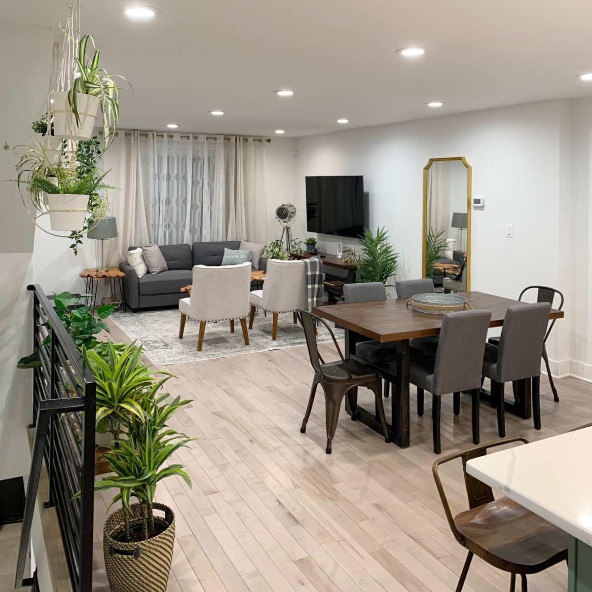 A modern open-concept living and dining area with a gray sofa, a dining table, and various plants throughout the space.