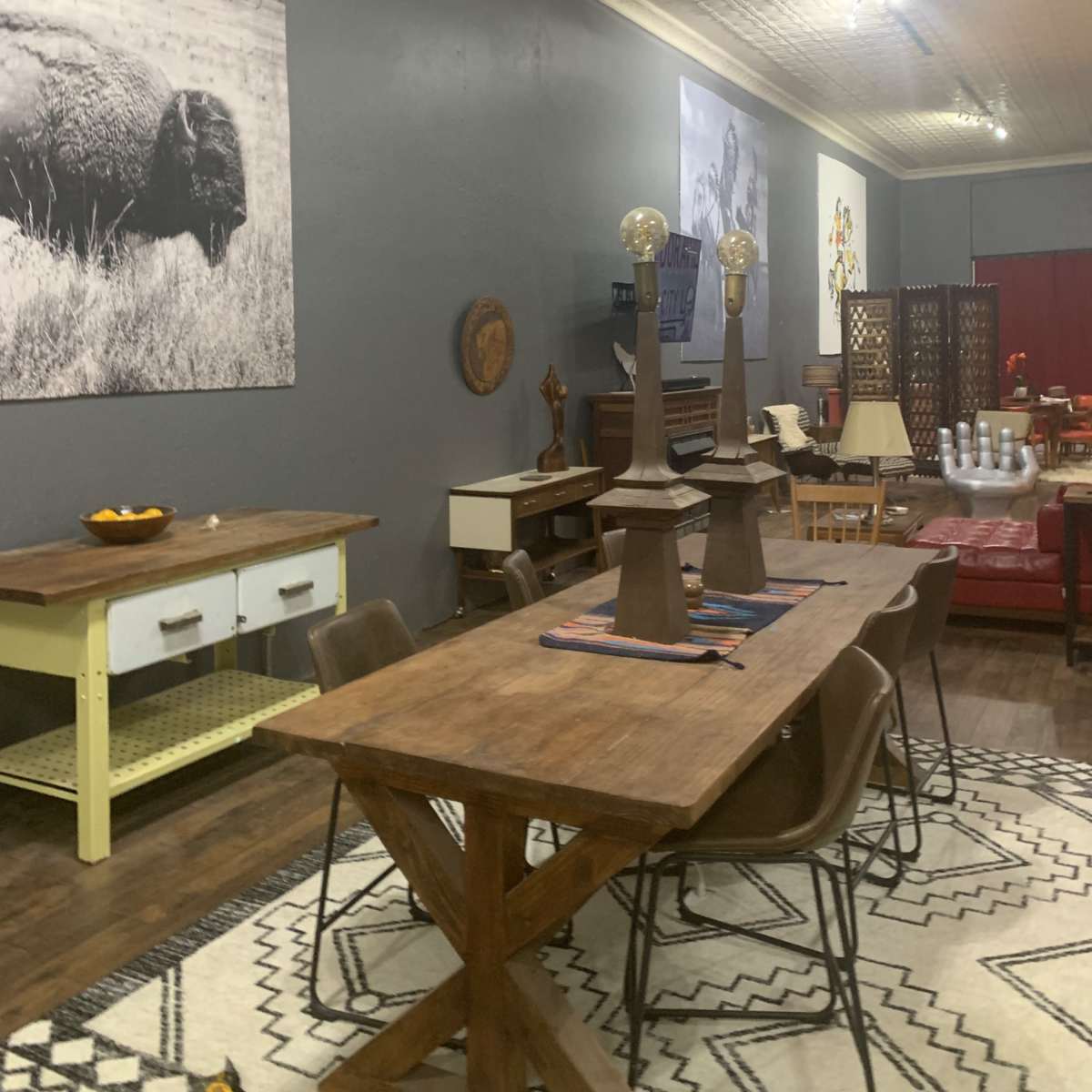 A spacious indoor area with a wooden dining table surrounded by chairs, large black-and-white photographs on the gray walls, and a mix of furniture items, including a piano and a decorative screen.