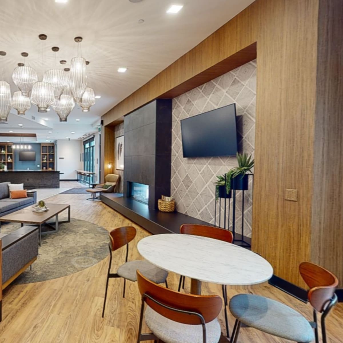 A modern, open-concept lounge area featuring a seating arrangement with a coffee table, a dining space, a television, and decorative lighting.