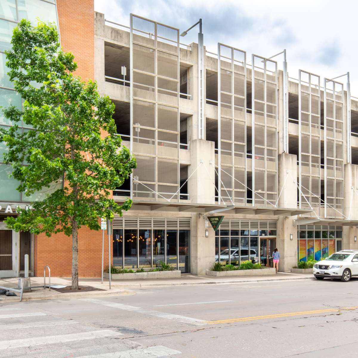 A modern parking garage building with a glass entrance and colorful murals on the side, situated on a city street.
