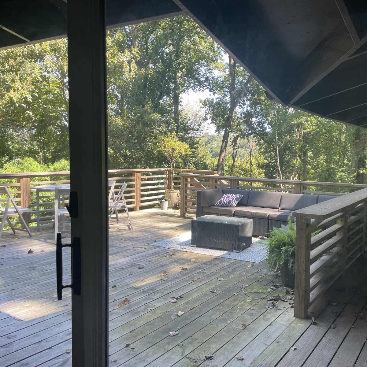 A wooden deck with a seating area and lush greenery in the background.