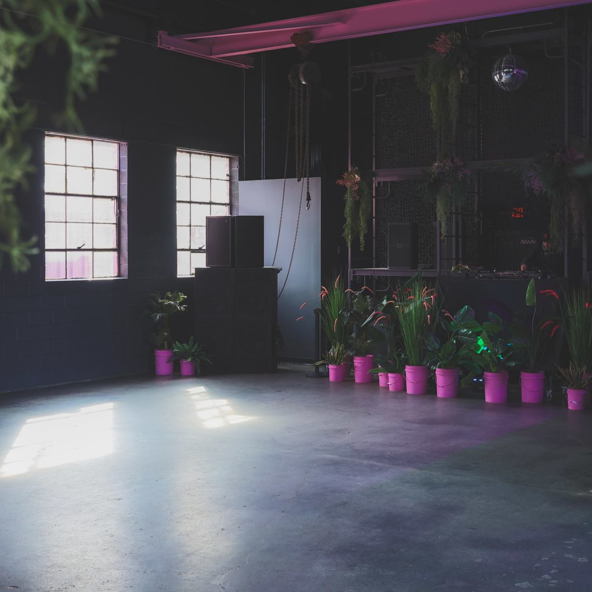 An empty indoor space with large windows, pink plant pots along the walls, and a sound system in the corner.