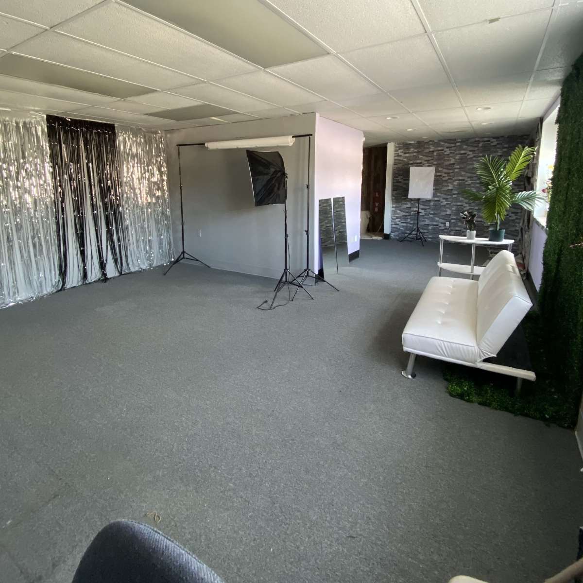 An empty studio space with a white sofa, a backdrop setup, and decorative elements including a green wall and shiny curtain.