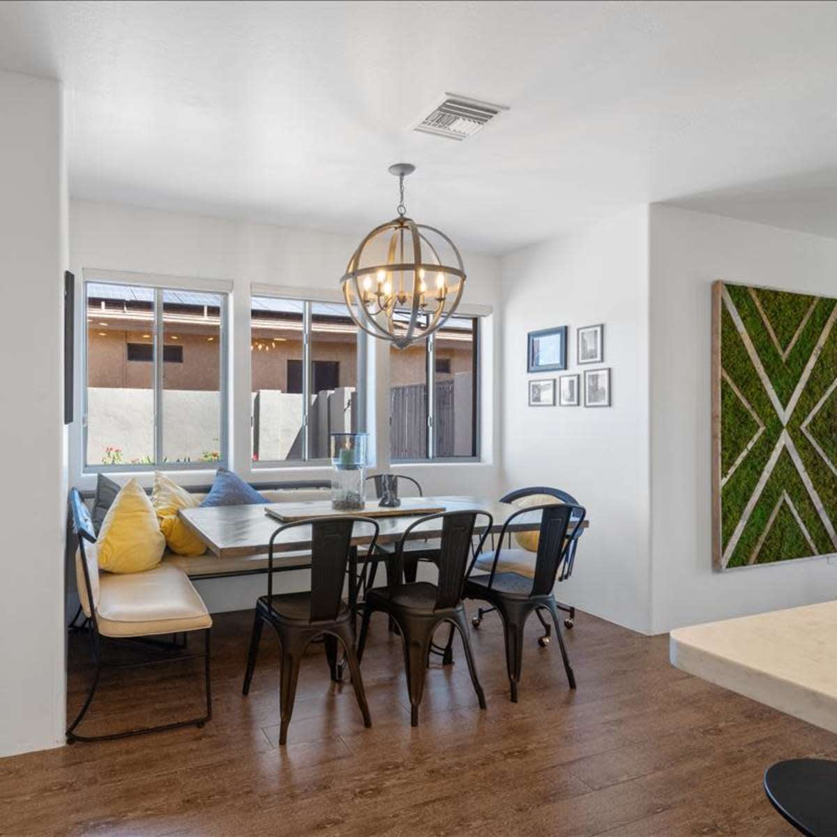 A dining area features a large table surrounded by chairs, with windows overlooking a patio and decorative wall art.