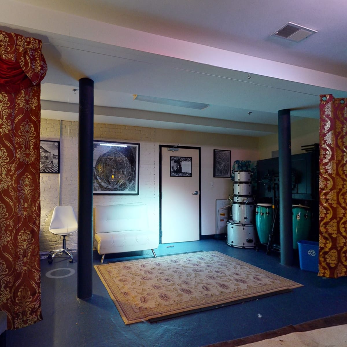 A room with red and gold curtains, a white chair, a couch, and musical instruments arranged against a wall.