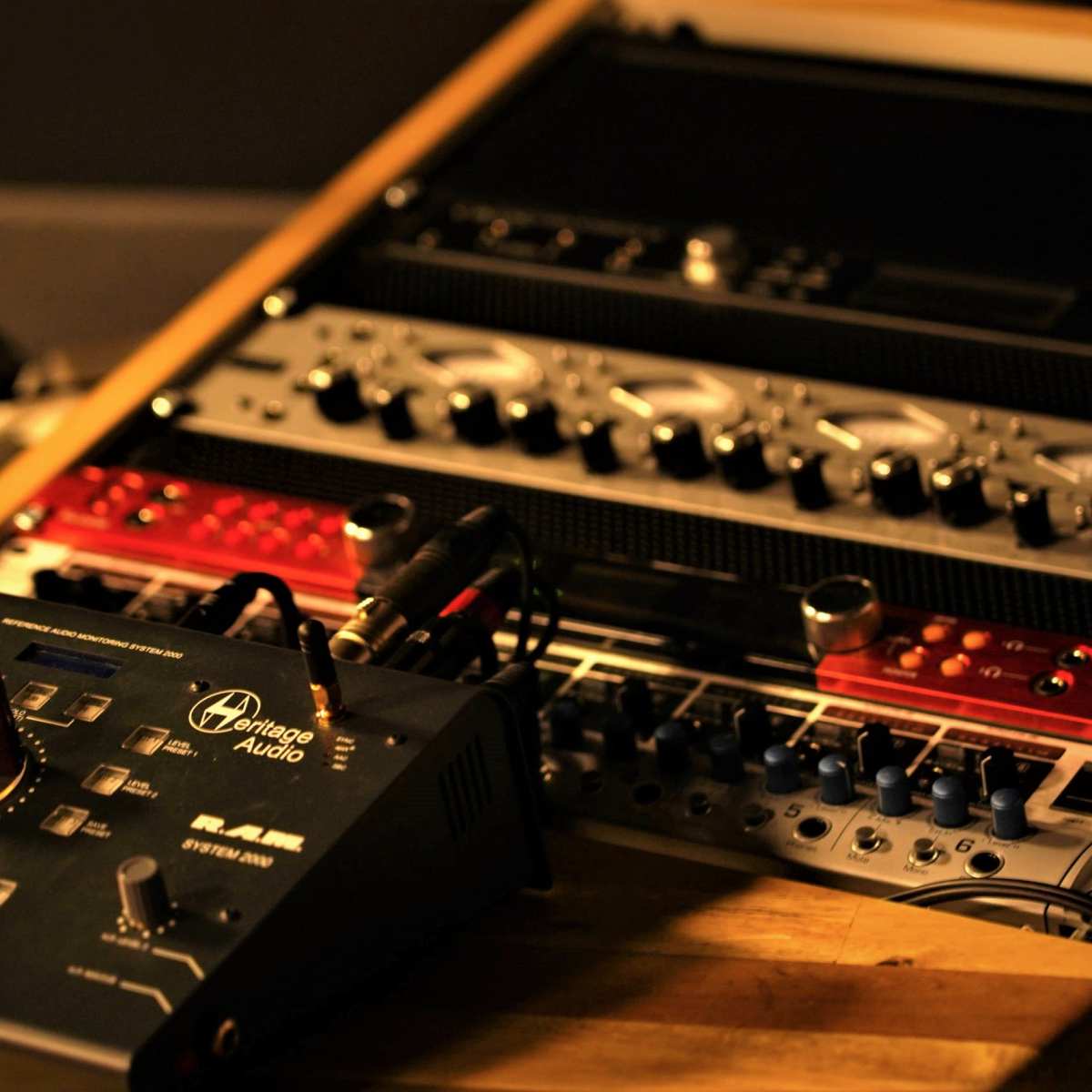 A collection of audio equipment, including a mixer and various rack-mounted devices, is arranged on a wooden surface.
