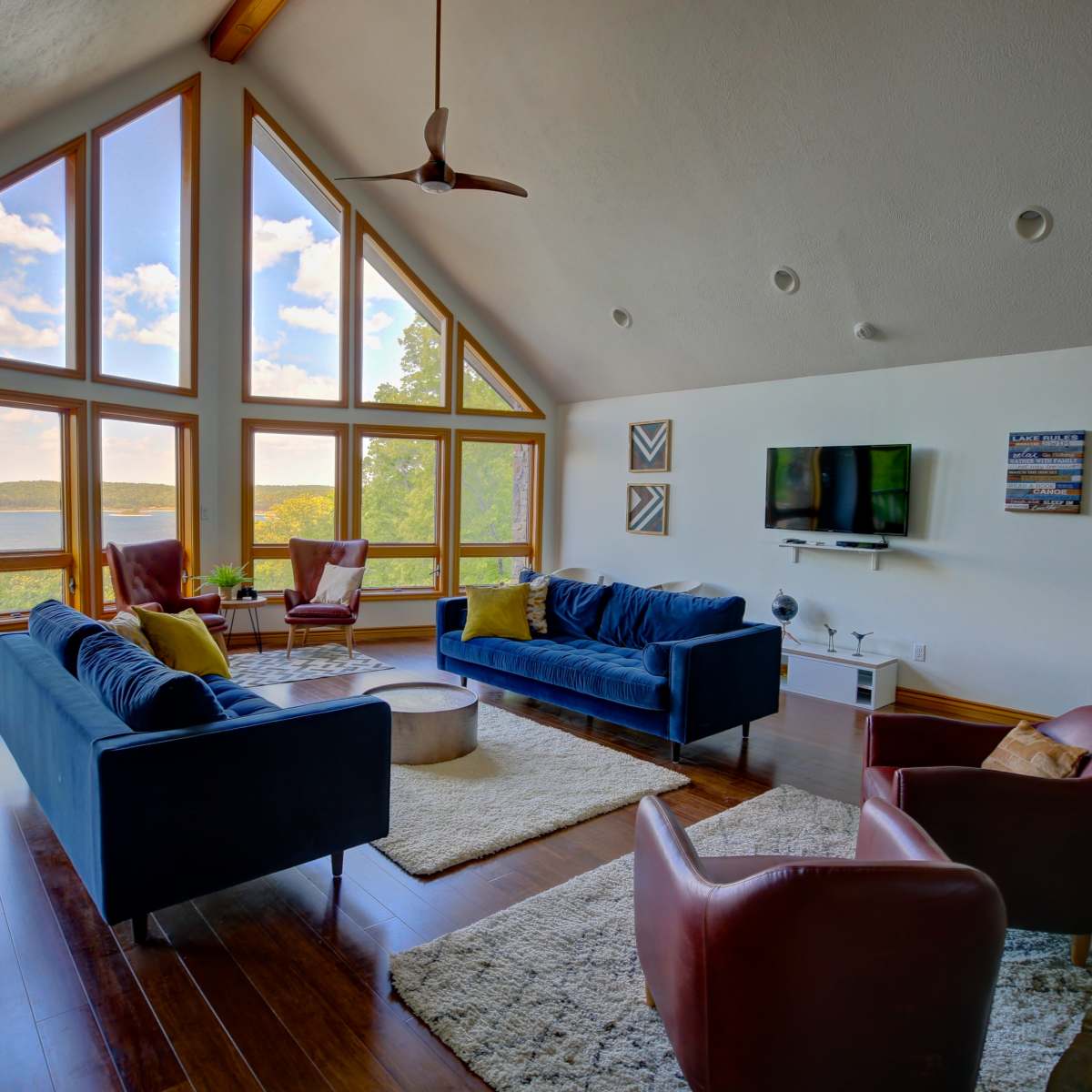 A spacious living room features large windows that offer a view of a lake and surrounding landscape, with two sofas, a coffee table, and a television.