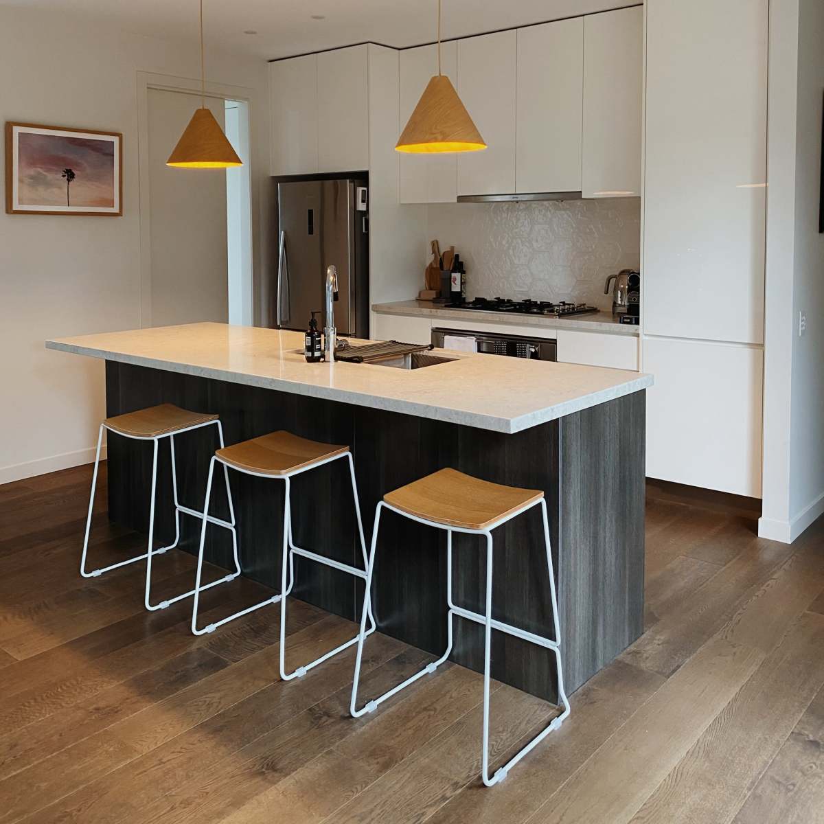 A modern kitchen with a central island, three bar stools, and pendant lights hanging overhead.