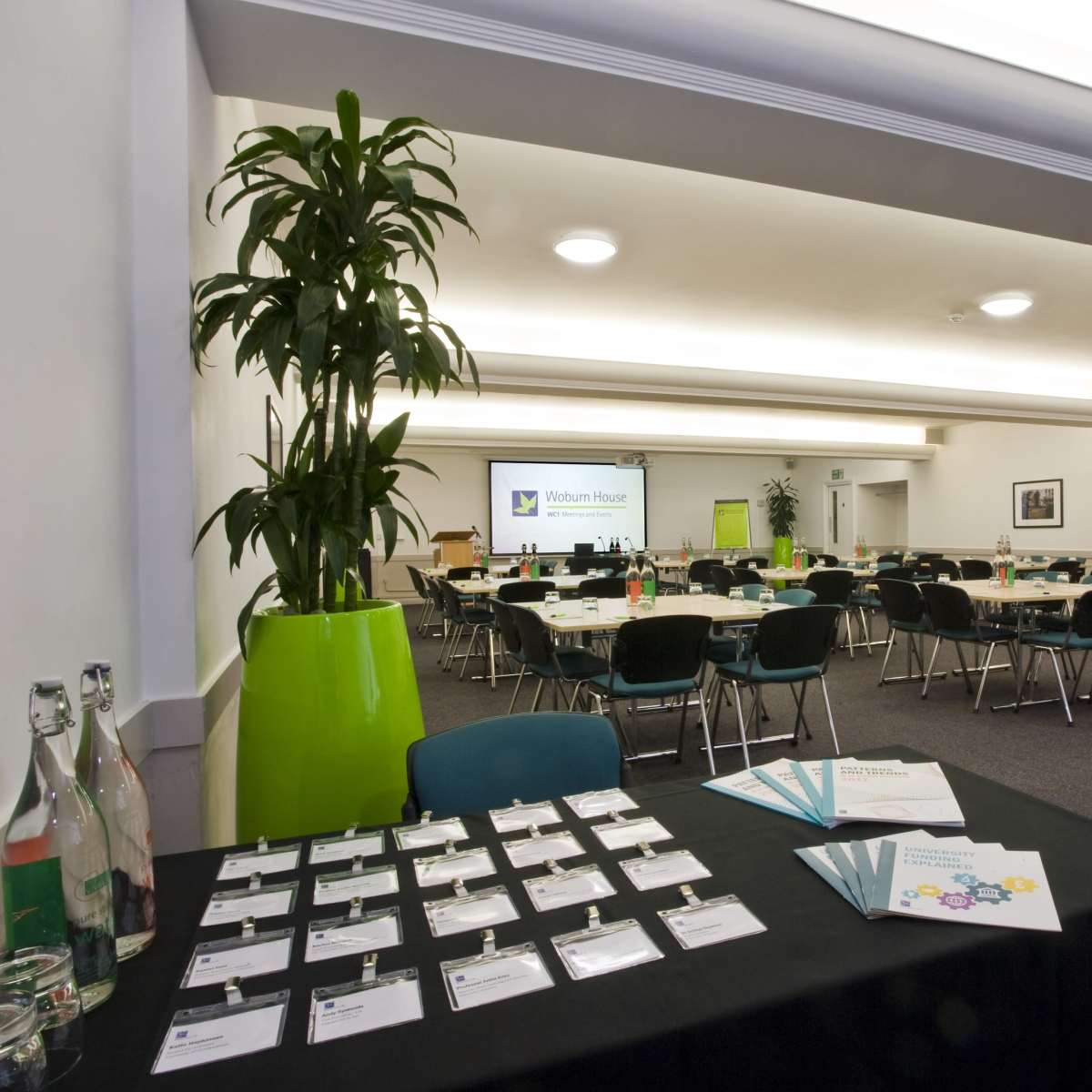 A conference room arranged with tables and chairs, featuring a registration table with name tags and a projector screen in the background.