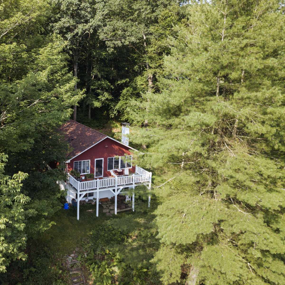 A small red house is situated on a wooden deck surrounded by dense green trees.