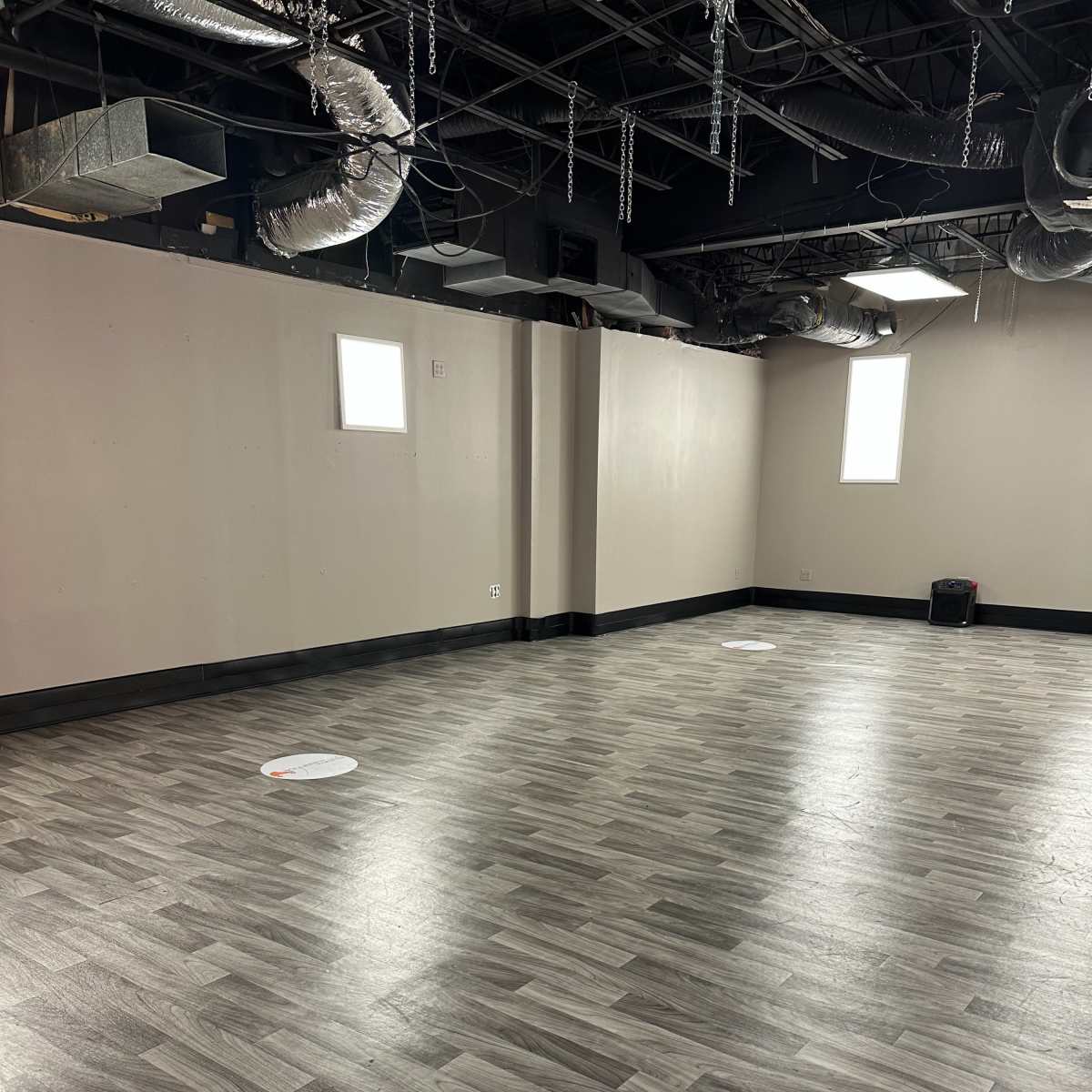 An empty room with gray laminate flooring, light-colored walls, and two circular markers on the floor.