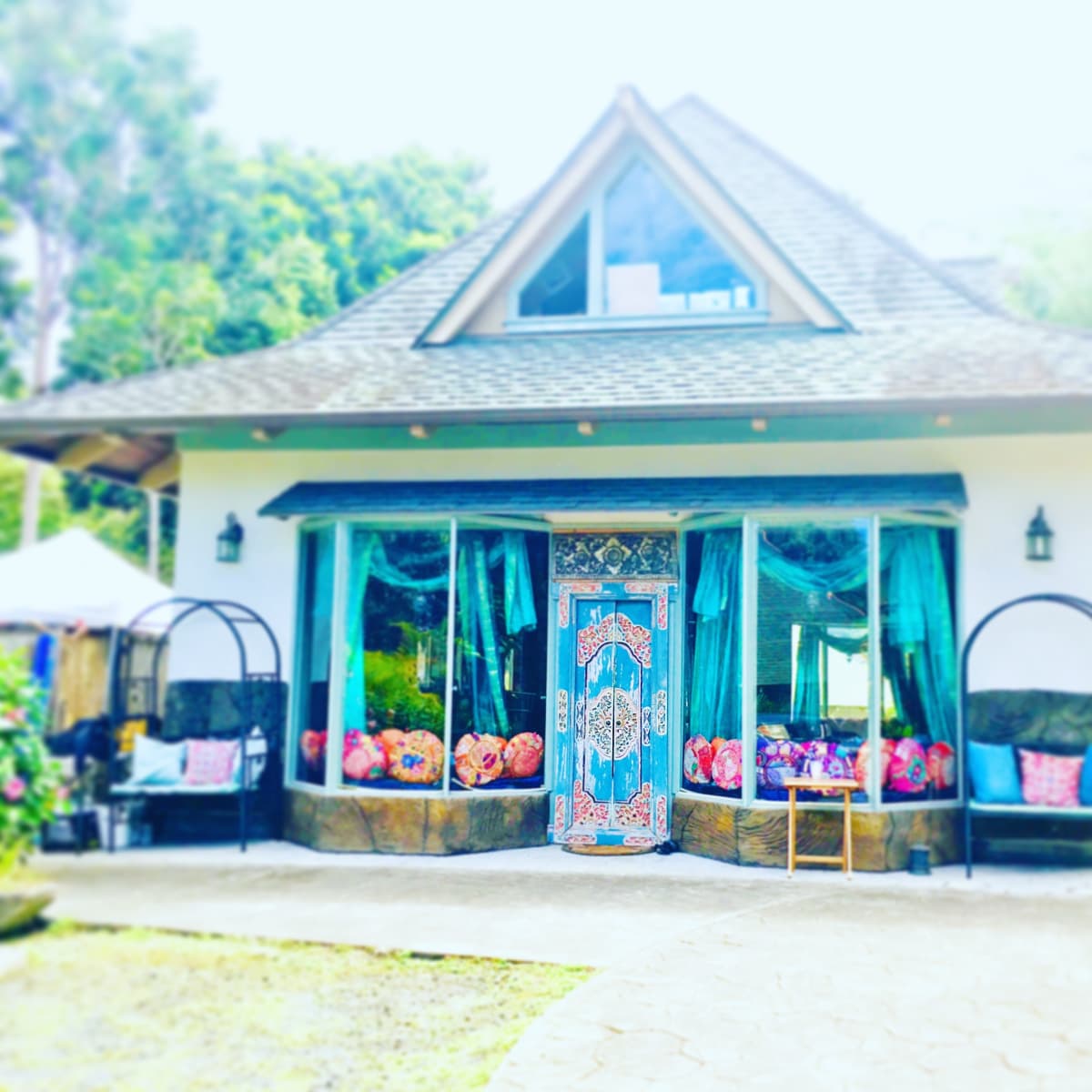 A charming house with a triangular roof and large windows, featuring decorated doors and colorful cushions on outdoor seating.