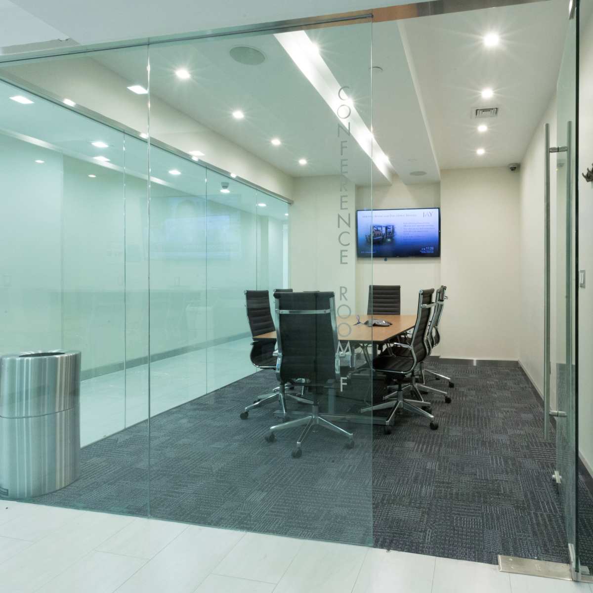 A glass-walled conference room with a round table and chairs is visible, featuring a television mounted on the wall.