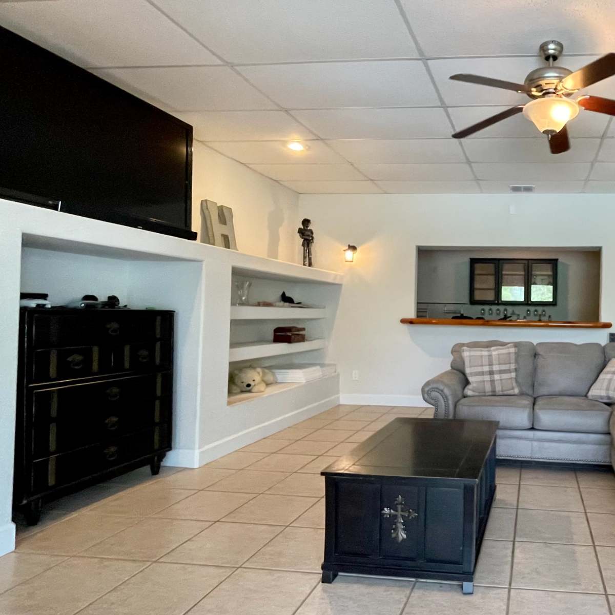 A living room with a sectional sofa, a coffee table, a flat-screen TV mounted on the wall, and built-in shelves displaying decorative items.