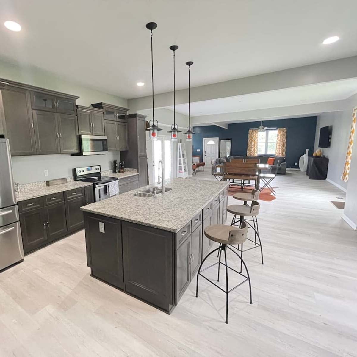 A modern kitchen with dark wooden cabinets, a large island with bar stools, and stainless steel appliances, all illuminated by overhead pendant lights.