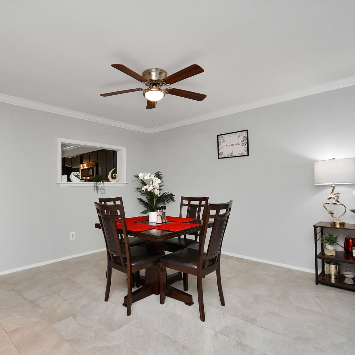 A dining area with a wooden table set for four, a ceiling fan, and a light-colored tiled floor.