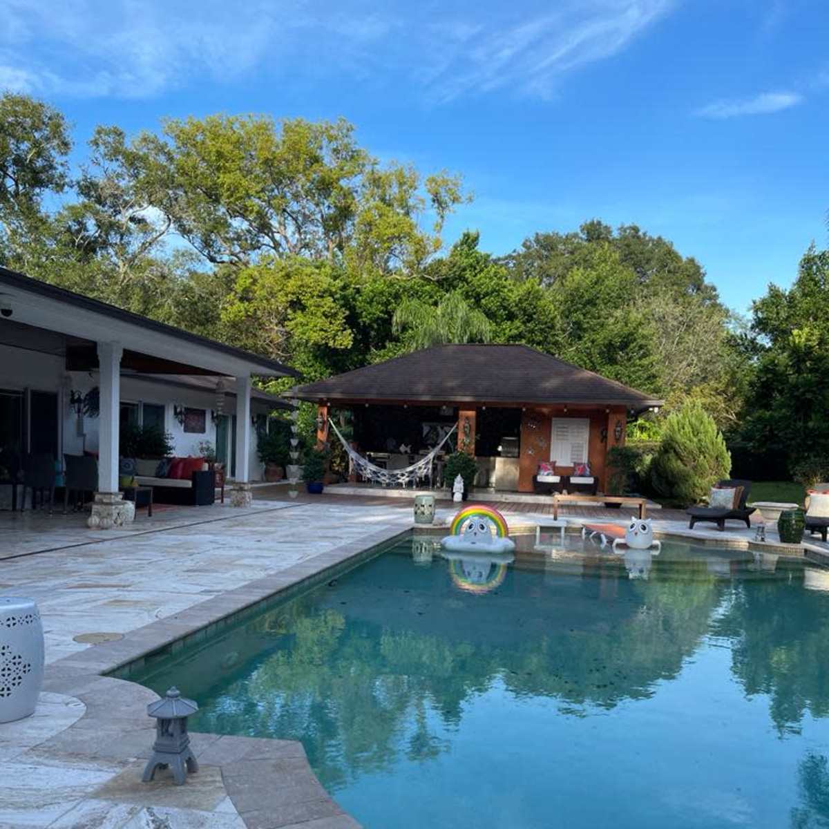 A residential backyard with a swimming pool surrounded by a patio and a gazebo in the background.